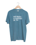 Blue t-shirt with 'The Magic is Already in You' text on a hanger against a white background