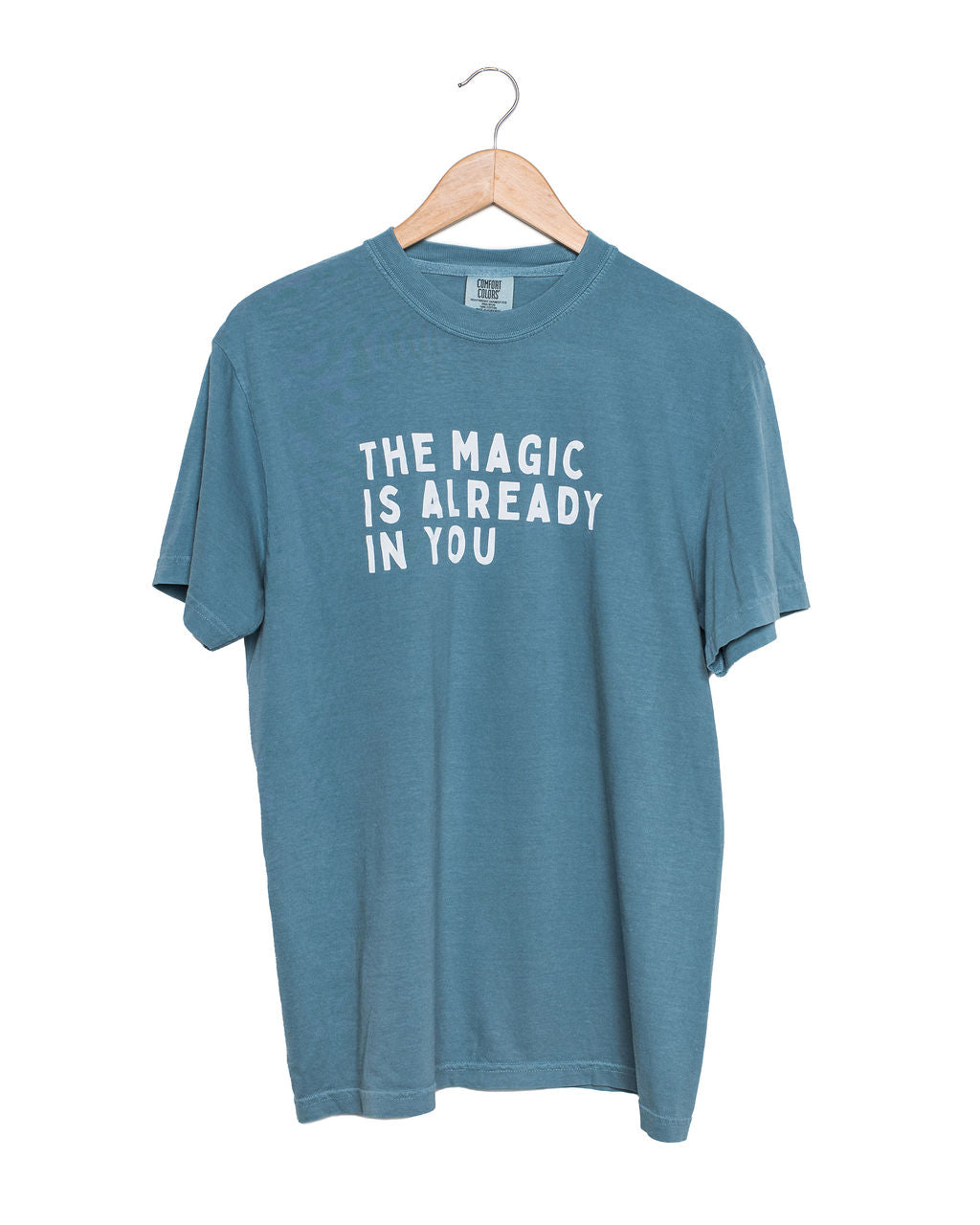 Blue t-shirt with 'The Magic is Already in You' text on a hanger against a white background