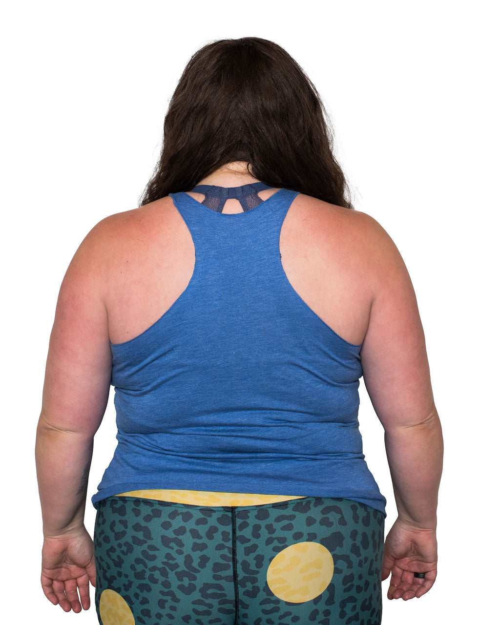 Mackenzie wearing a blue tank top showing the back view of the racerback tank and patterned leggings on a white background